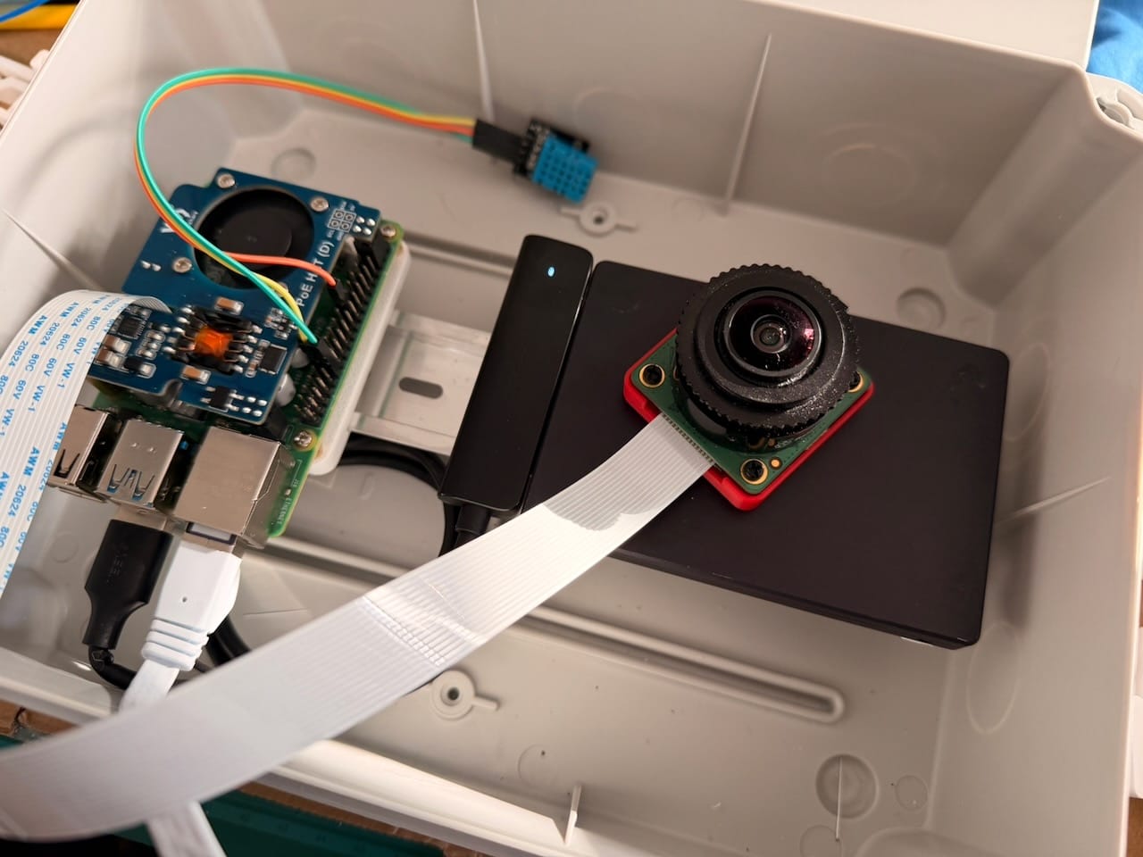 A Raspberry Pi 4, SSD, humidity sensor and the HQ camera with its fisheye lens, test-fitted inside the weatherproof junction box