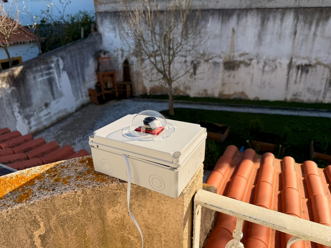 The completed allsky camera in its weatherproof enclosure, mounted on a wall on the roof terrace with terracotta tiles and a garden behind